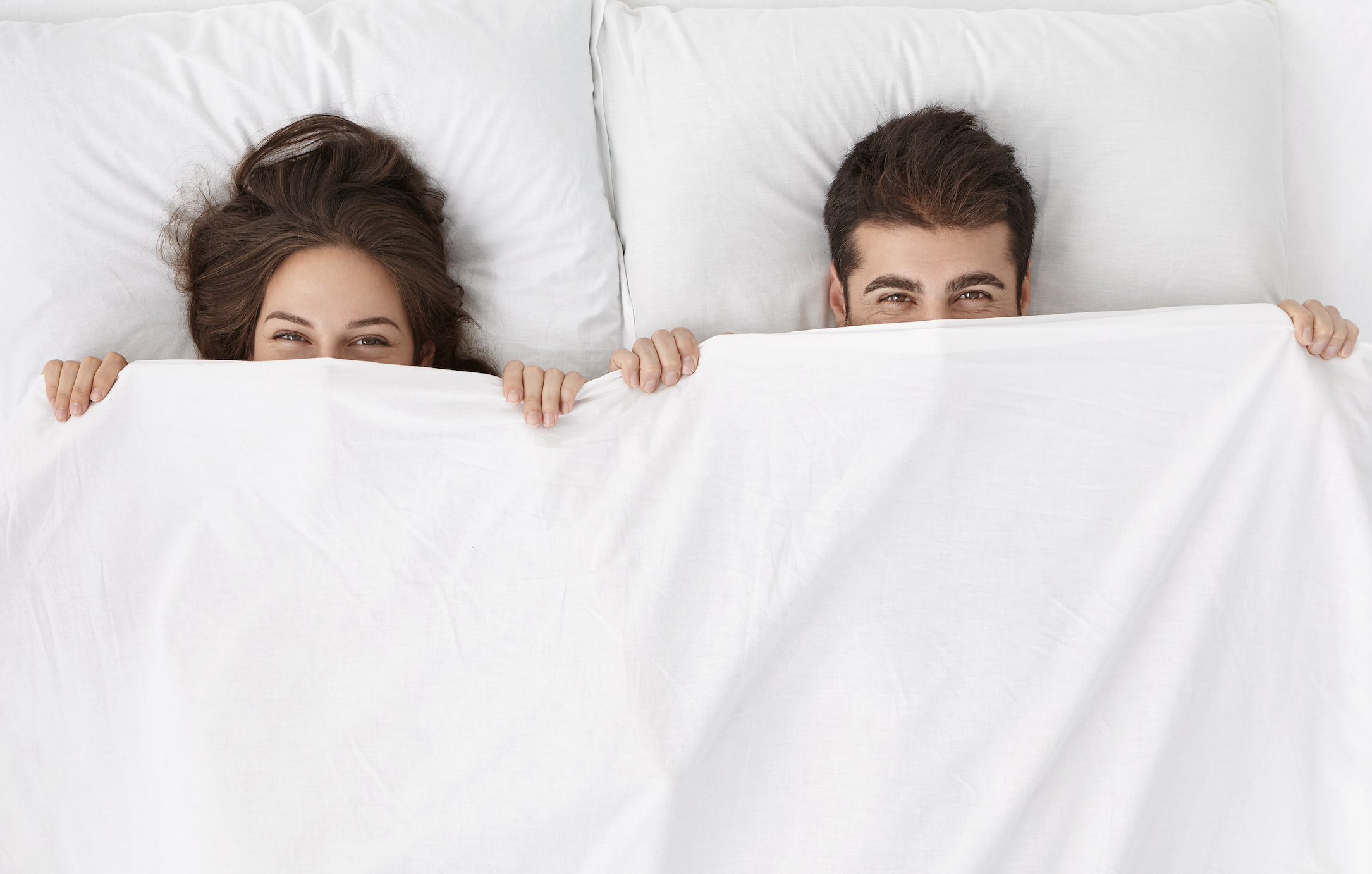 couple under white bed sheets smiling