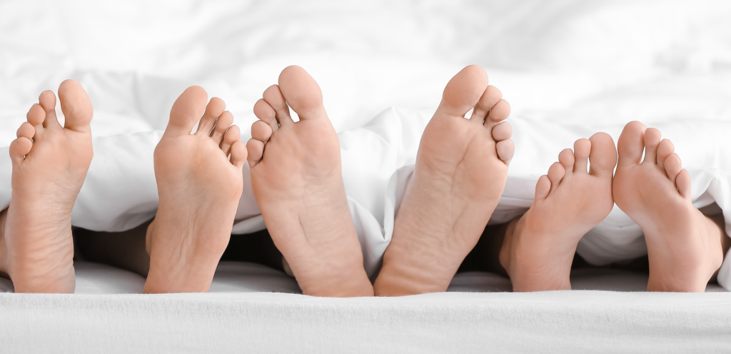 3 pair of feet popping out from white bedsheets